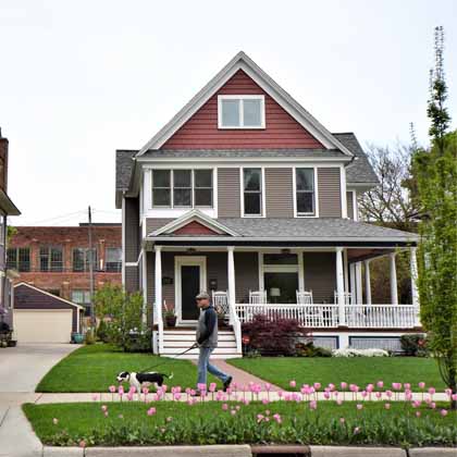 man walking dog on street in front of nice porch on home