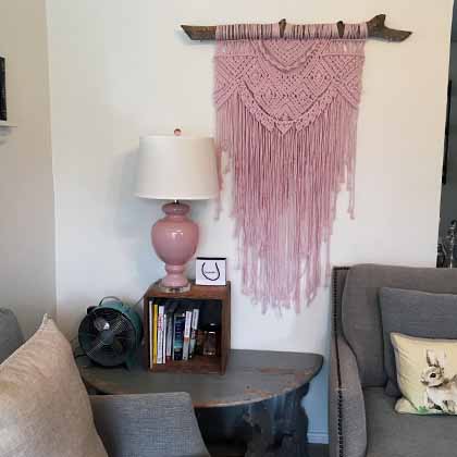pink macarame hanging on the wall with a little fan beside it