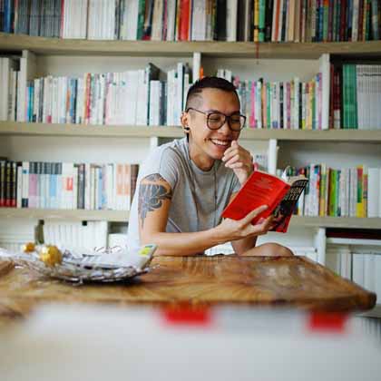 person sitting at home desk reading with bookshelves behind them