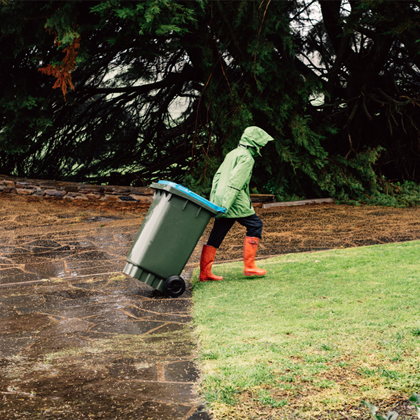 person in rain coat and rain boots taking out the garbage