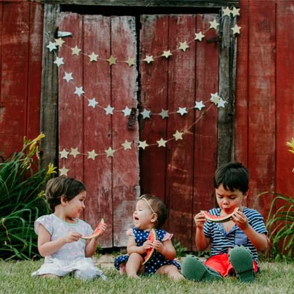 three toddlers sitting outside in the grass eating watermelon