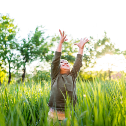 child raising arms to the sky in a green field
