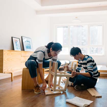 two young adults sitting on floor of empty apartment building stool