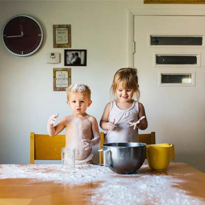 two children making a mess in the kitchen with flour