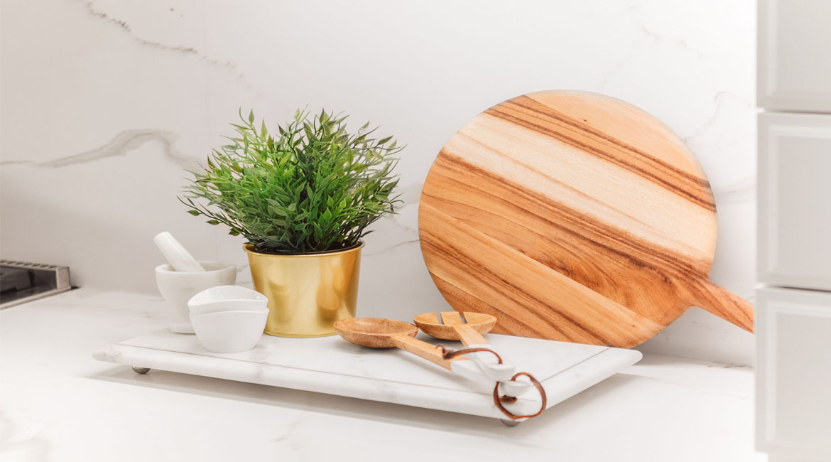 A cutting board, mortal and pestle and a plant on a kitchen counter.