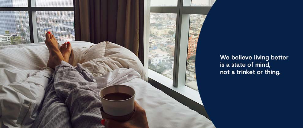 person in bed with coffee looking out window at city views