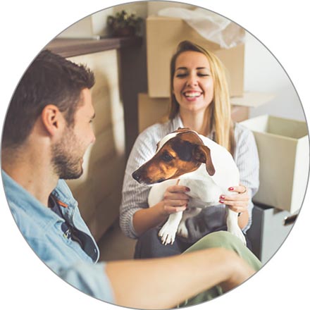 A young smiling couple and their Jack Russell Terrier sit on the floor of their new kitchen, surrounded by boxes.