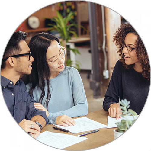 A young couple happily talk to a Minto Sales Representative over a Site Plan table in a Minto Sales Centre.