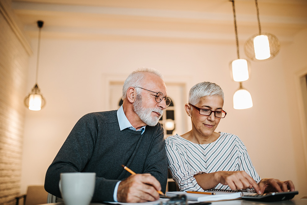 An elderly couple smile as they sit together and go over their finances.