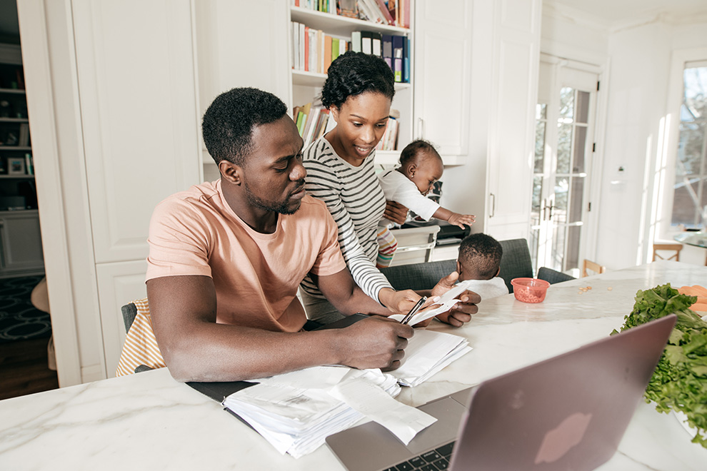 A young family of four sits at their kitchen counter going through paperwork and researching mortgaging options for their new home purchase.