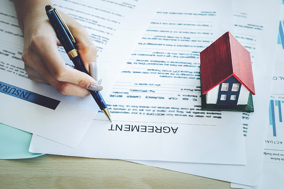 A woman with long acrylic nails signs her mortgage agreement paperwork.