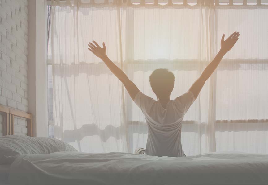 man sitting up in bed with his arms up 