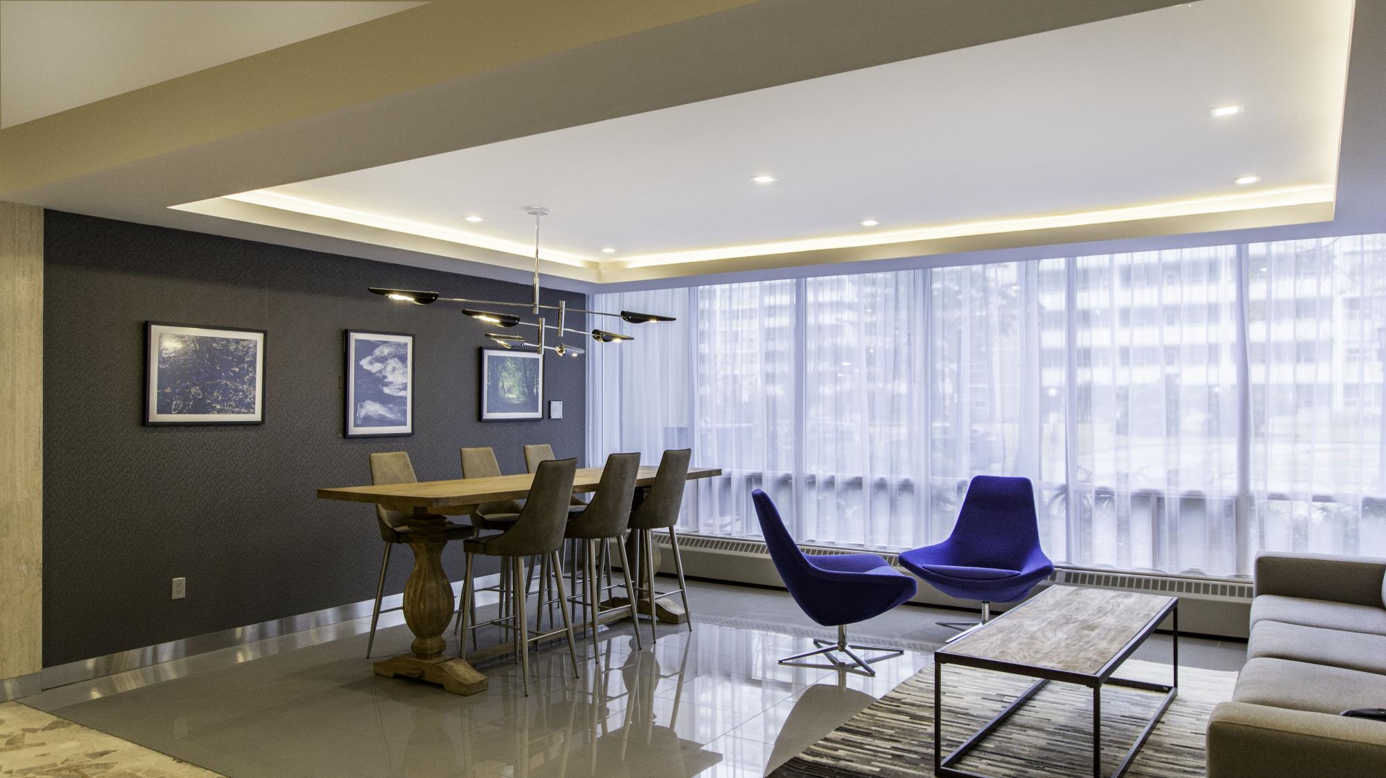 Lobby at an apartment building with blue chairs and a wooden table with high chairs surrounding it 
