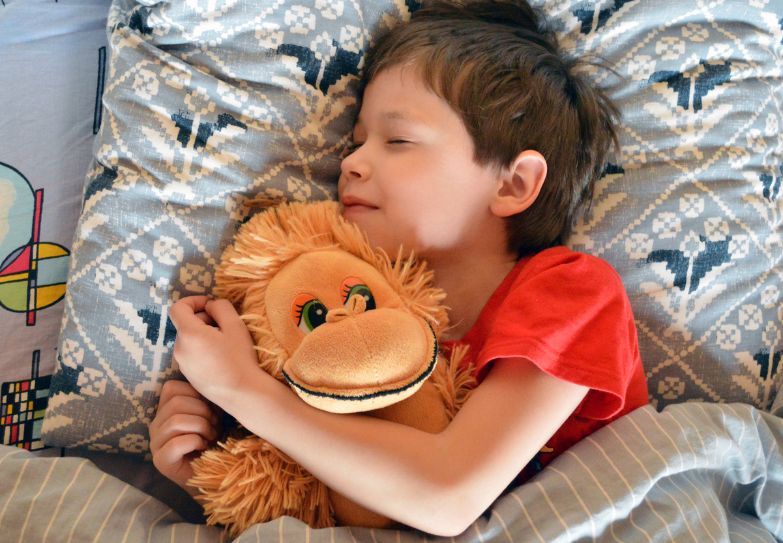 Child holding teddy bear in bed