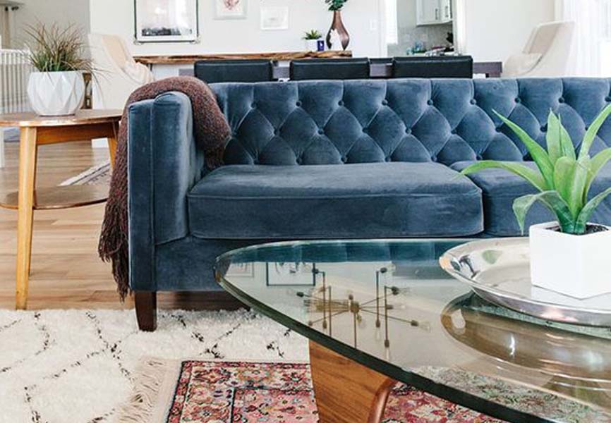 Blue sofa on top of layered rugs, the bottom rug is white and the rug on top was red