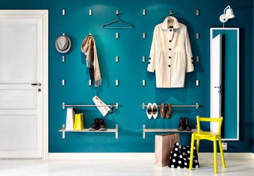 Blue dark walls with hooks all over the wall to hang hats and coats with a yellow chair next to the wall