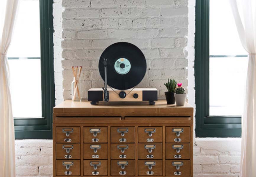 A record player against a white brick wall situated in between two windows