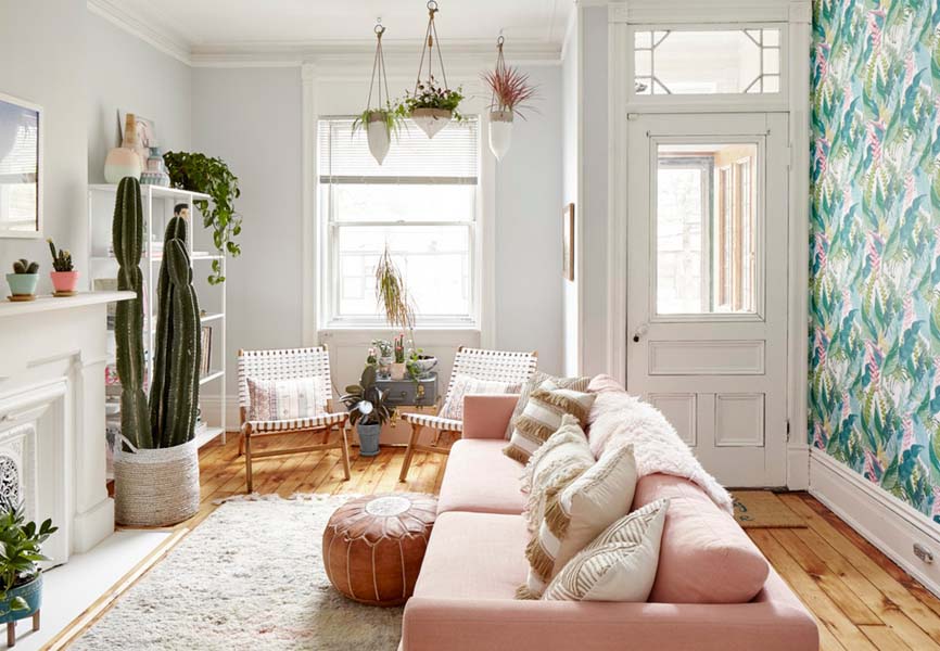 Pink sofa in a white room with plants hanging around the window 