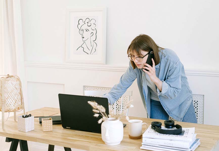 Woman in jeans and shirt talking on a cellphone in a home office