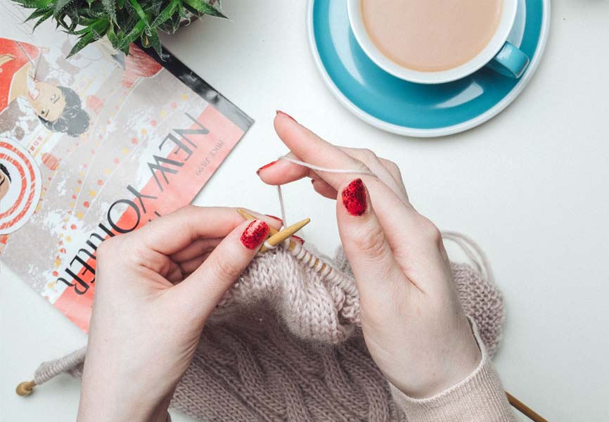 A girl with red nails knitting and drinking coffee