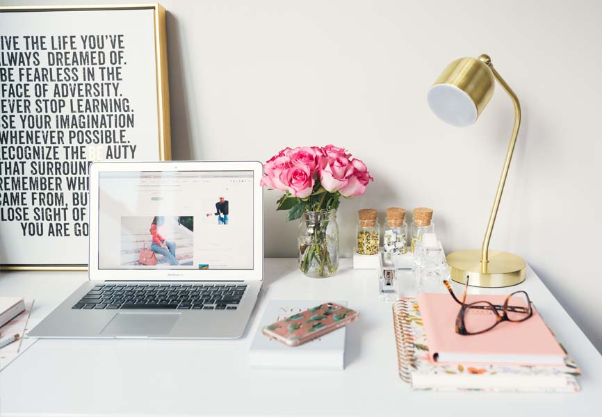 desk with a gold lamp, a mac book pro and pink flowers