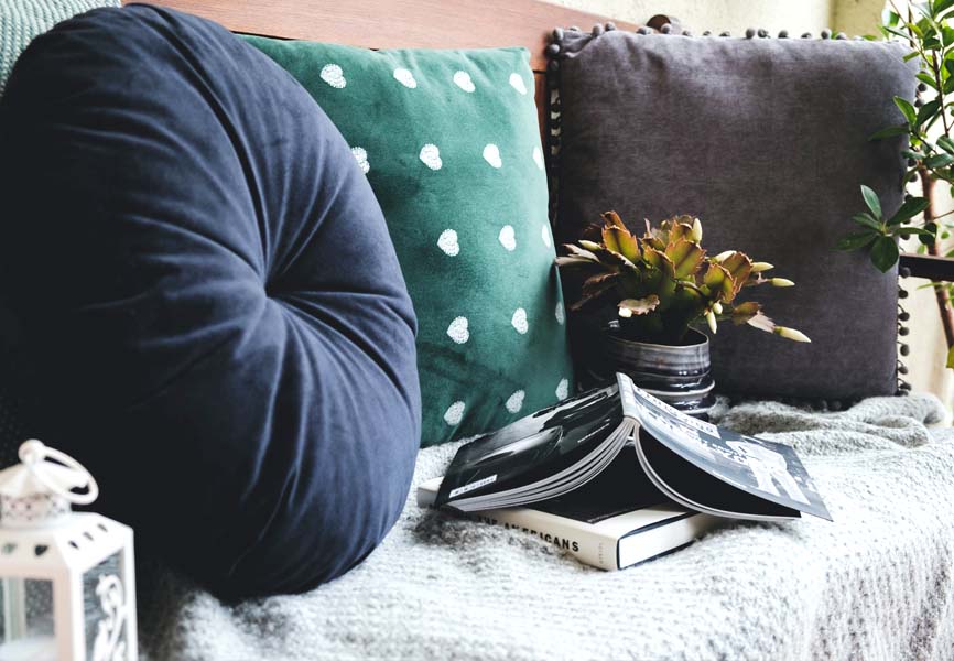 pillows and throws with books piled up on a bench
