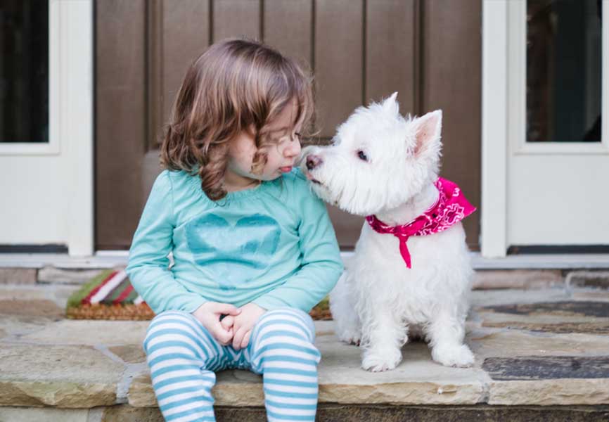 Little girl sitting next to a small white dog