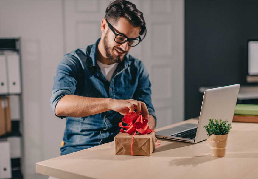 young man sitting at table wrapping gift with red bow