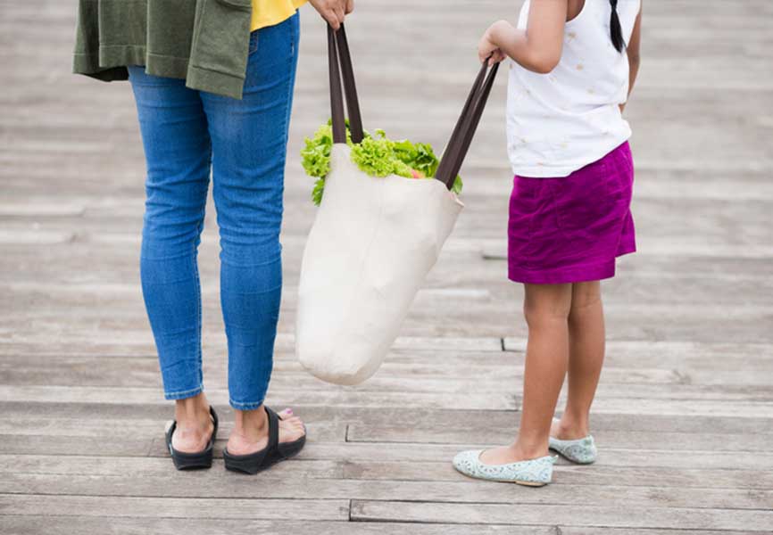 Mother and daughter holding a full reusable grocery bag