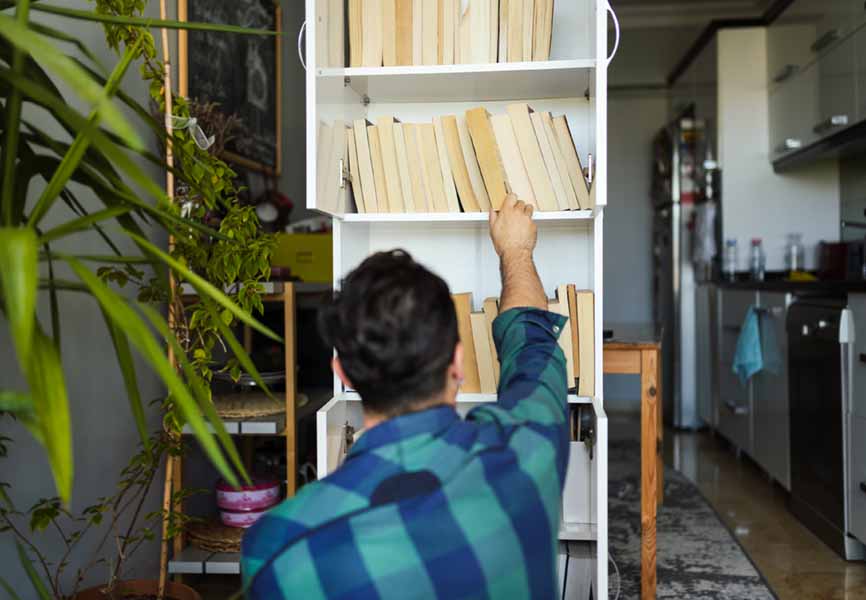 person filling a large bookshelf with books