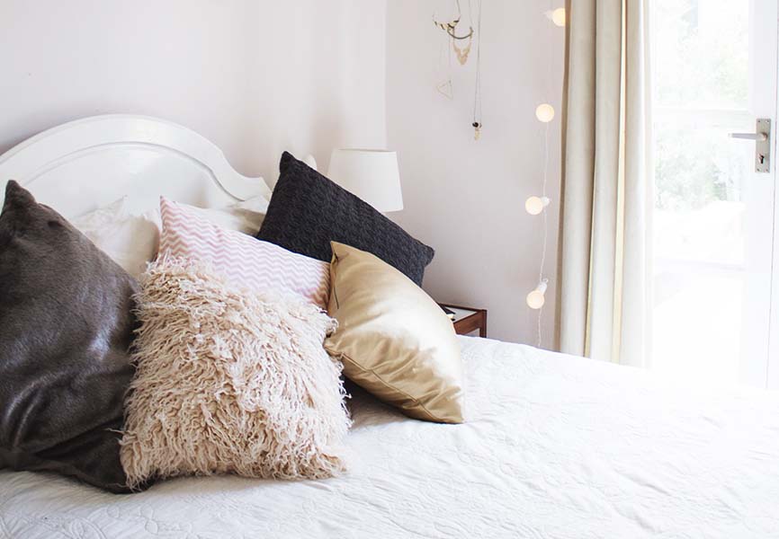 cozy white bed with fluffy white and grey pillows and string lights