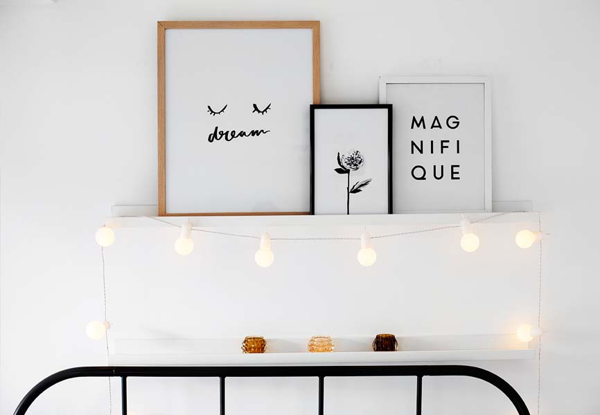 white bedroom with shelf over bed frame with cute framed pictures and string lights