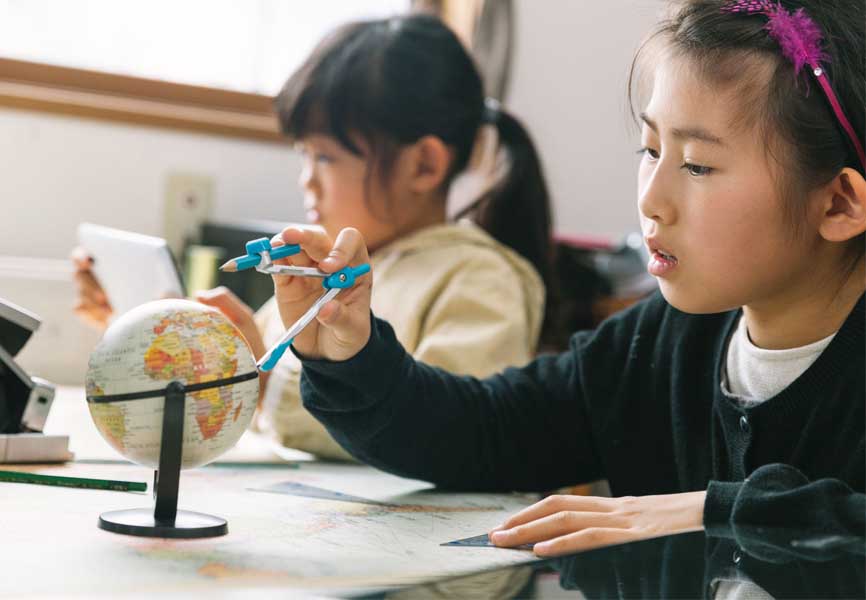 two young girls in school with world atlas