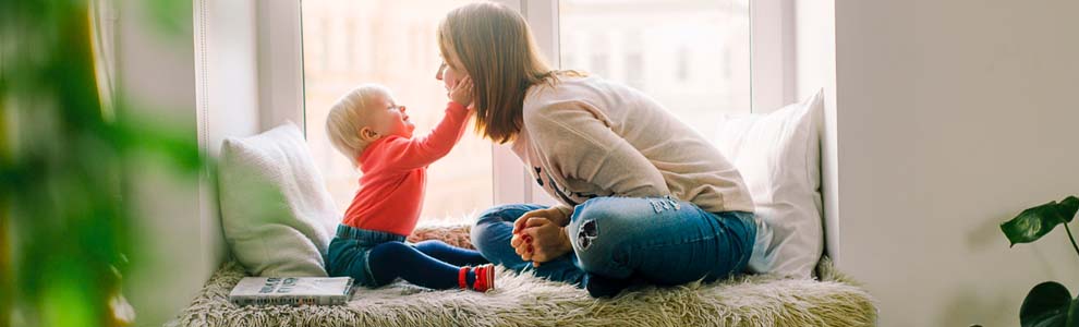 Baby sitting on window sill, reaching and touching moms face