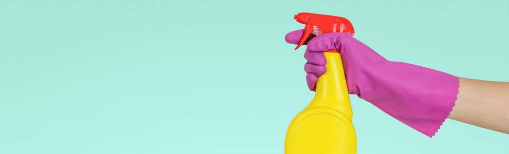 Hand covered in a purple glove holding yellow cleaning bottle